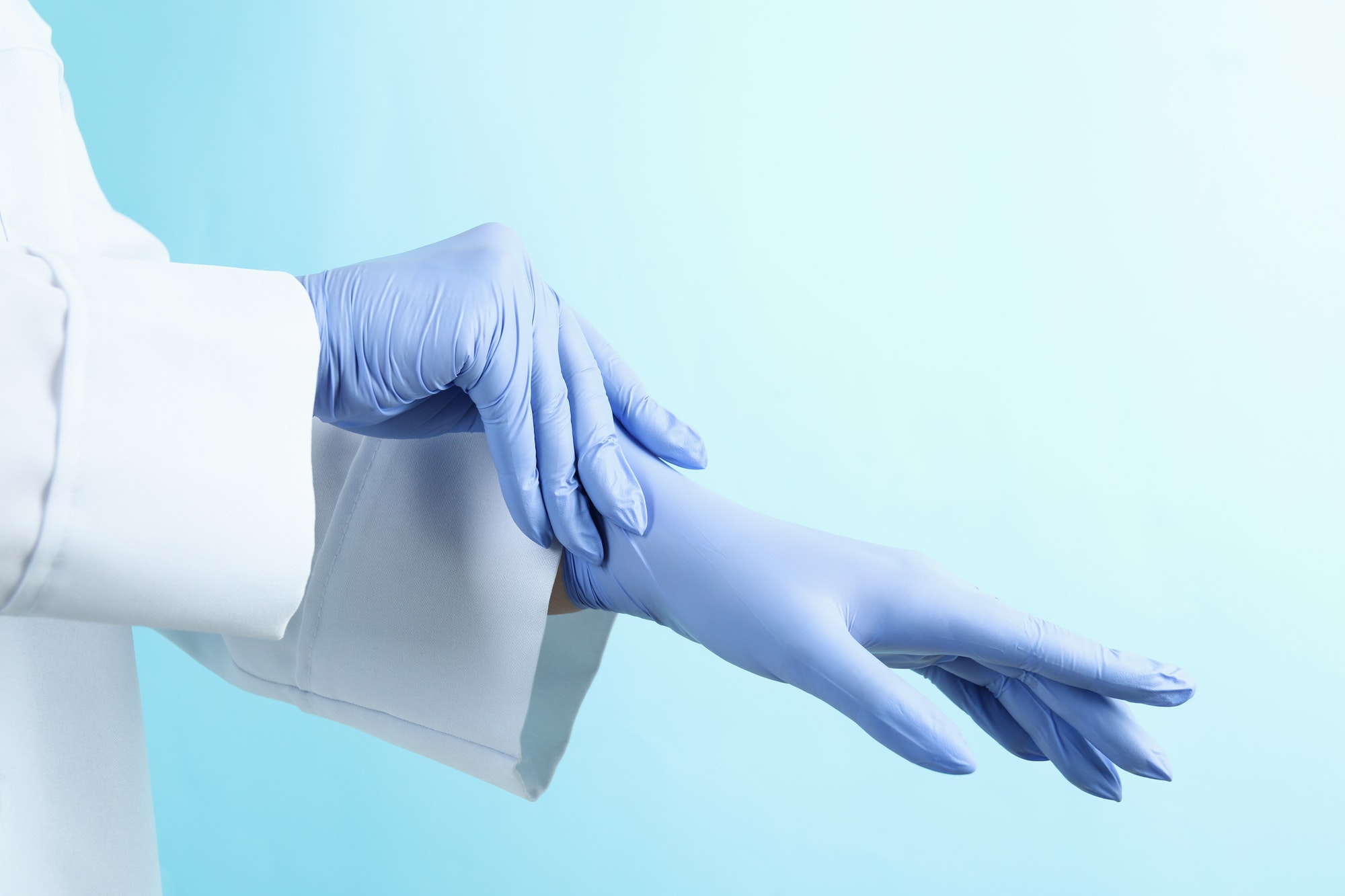 Doctor putting medical gloves on blue background